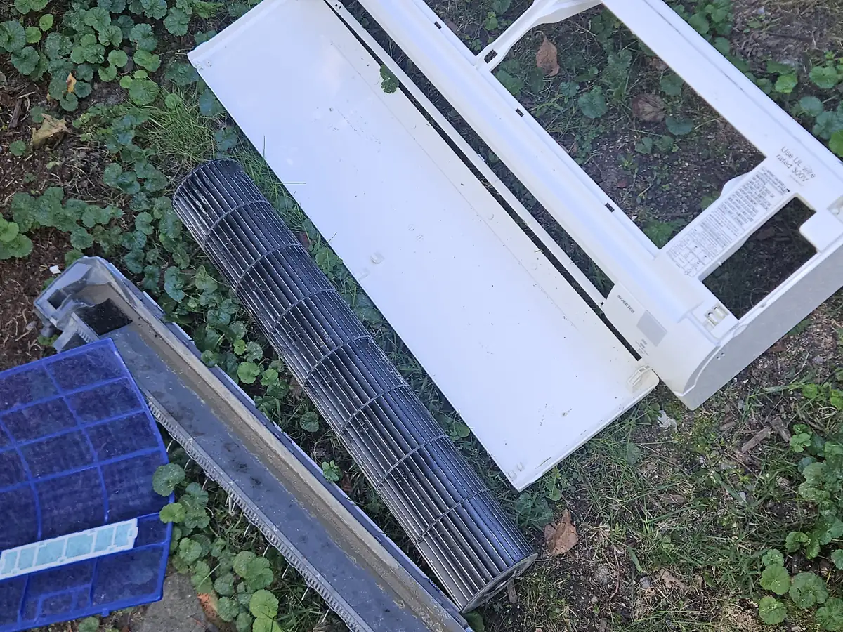 Mini-split cover, drain pan, blower wheel and filters laid out on the grass for washing in Brighton, MA