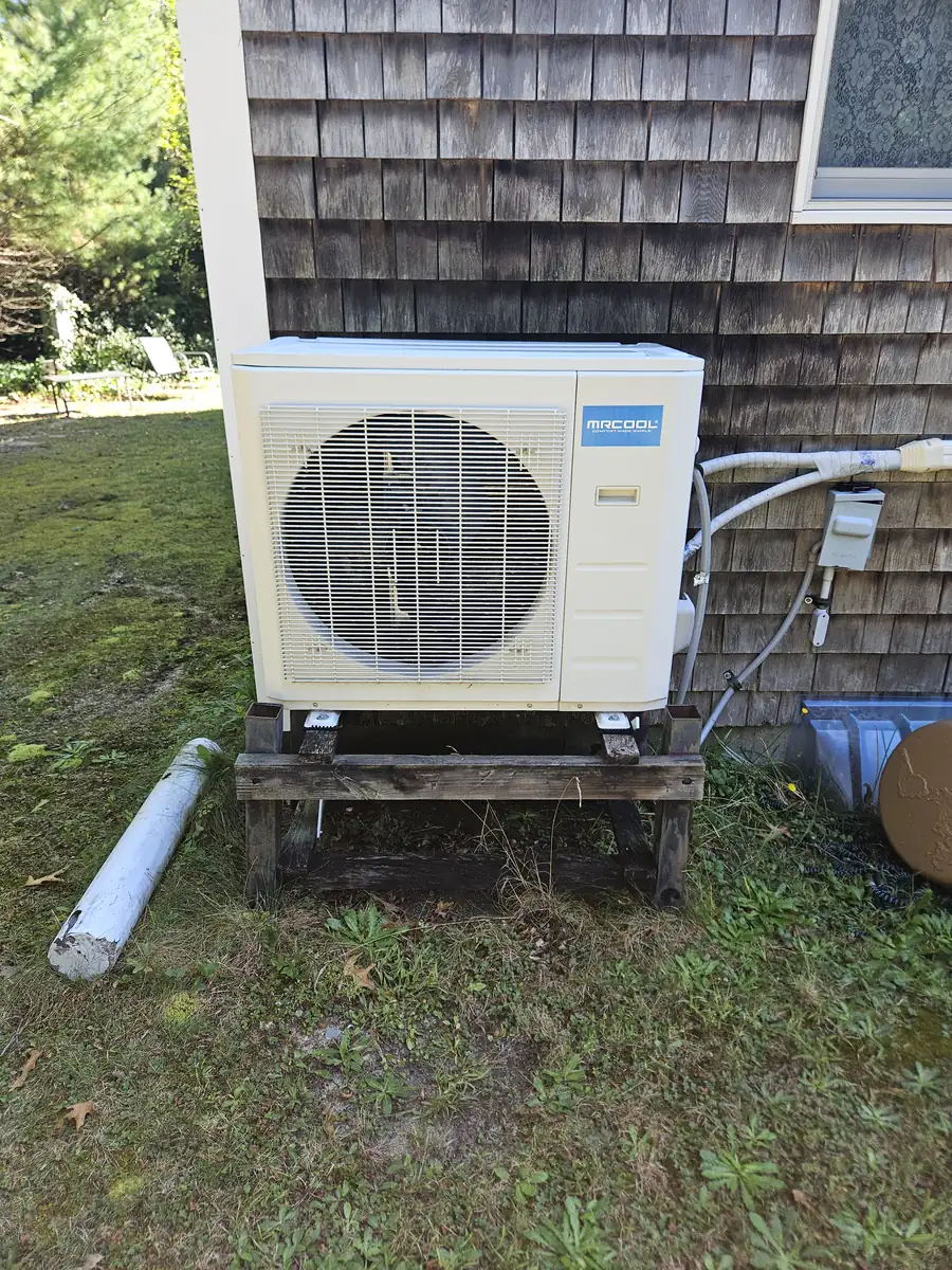 MRCOOL outdoor condenser on a wood pad beside a shingled Cape home in Falmouth, MA