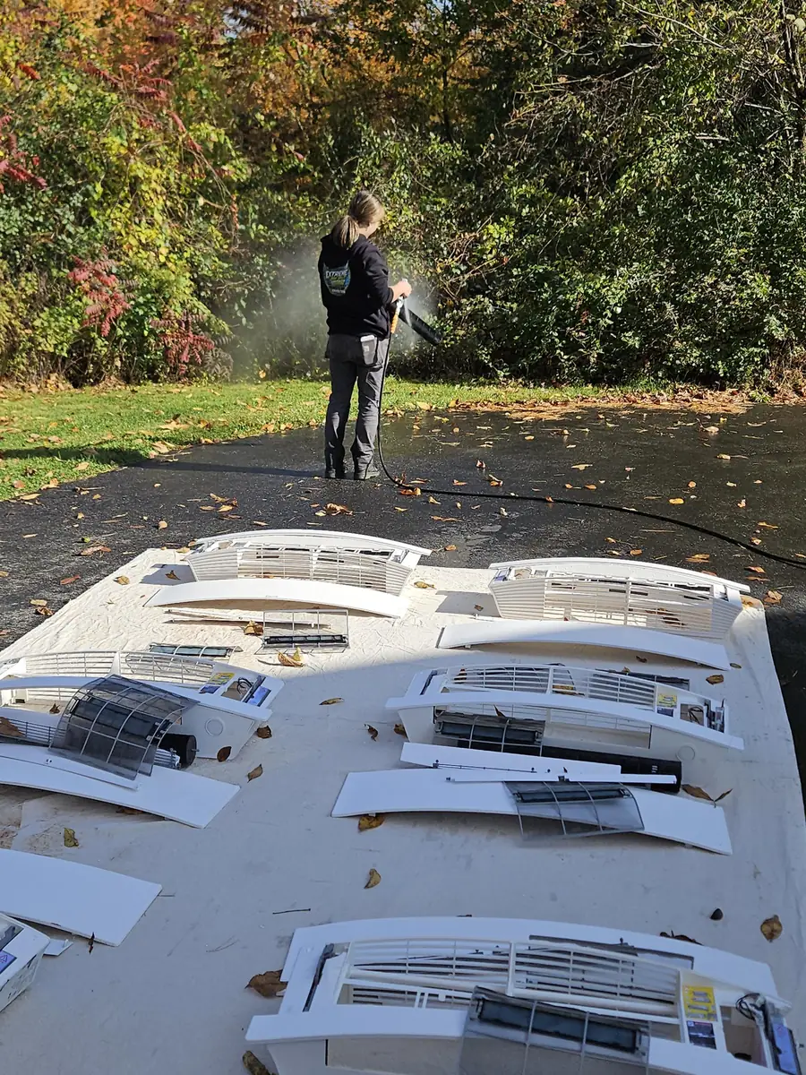Technician pressure washing mini-split covers, grilles and blower wheels in the driveway of a Pepperell, MA home